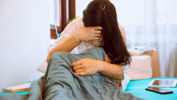 eine Frau ist zu sehen, die im Bett sitzt und sich den Kopf hält.