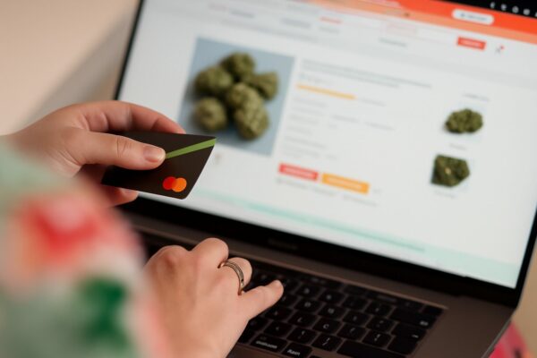 Online Verschreibung von Cannabis Blüten bald nur noch erschwert möglich ? Hier sieht man eine Person, die Online mit einer Kreditkarte in der Hand Cannabisblüten bestellt.