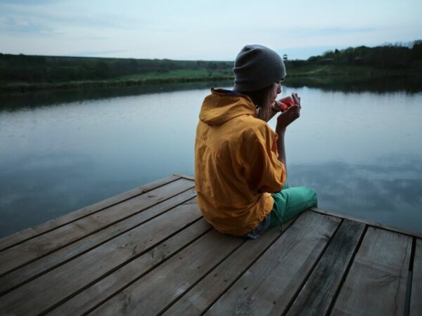 Cannabisstrafen bei Jugendlichen. Ein junger Mann sitzt auf einem Steg an einem See und zündet sich einen Joint an.