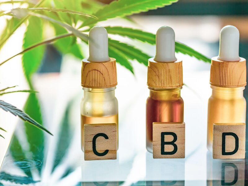 CBD aus der Apotheke: Drei Fläschchen mit CBD und eine Hanfpflanze