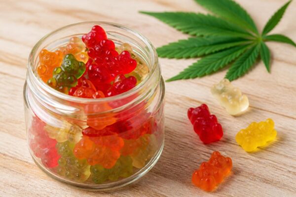 CBD Gummibärchen in einem Glas neben einem Hanfblatt