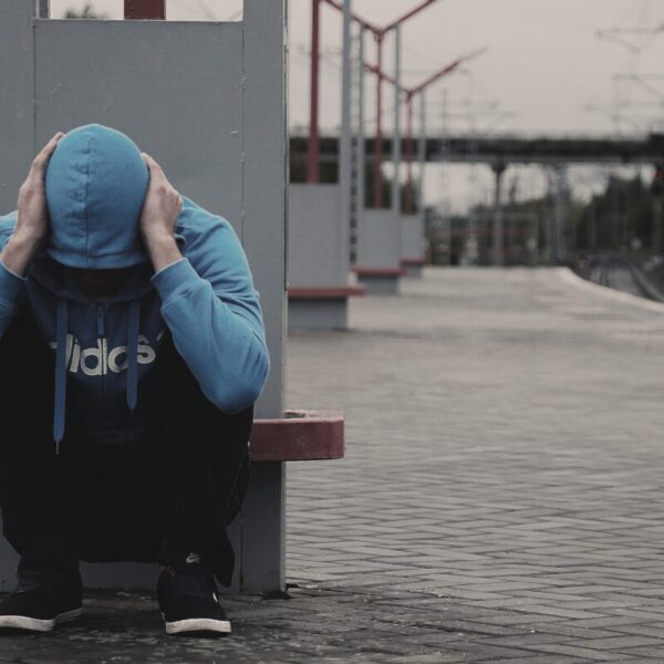 CBD gegen Angst. Ein Mann mit Kapuze hält sich den Kopf und sitzt an einem Bahnsteig.